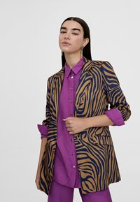 Blazer with a blue and brown zebra print design, featuring a tailored shape and structured shoulders, paired with a solid purple shirt.