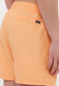 Narancssárga úszóshort, rugalmas derékkal, hátsó zsebbel és egy kis fekete márkalábbal. Sima, könnyű anyag.