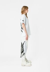 Camiseta blanca oversize con bordado de alas negras, combinada con joggers blancos que presentan un bordado detallado. Estilizada con botas gruesas blancas.