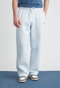 Ανοιχτό μπλε φόρμας από μαλακό ύφασμα με ελαστική μέση και κορδόνι, καθώς και πλαϊνές τσέπες· περιλαμβάνει μικρή λεπτομέρεια με λογότυπο.