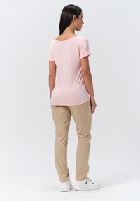 Top rosa de manga corta con escote redondeado, combinado con pantalones beige, llevado con zapatillas blancas. Textura suave, ajuste casual.