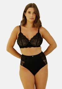 Ensemble de lingerie noire comprenant un bralette en dentelle transparente avec des bords festonnés et un bas taille haute avec des accents en maille et un bouton décoratif.