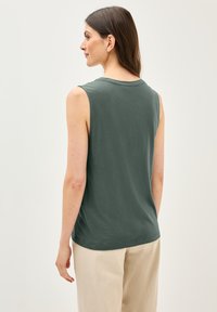 Top verde sin mangas hecho de tela suave, con escote redondo y corte relajado, combinado con pantalones beige claros.