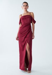 Bordana satenska haljina s dekoltiranim rukavima, pripijenim gornjim dijelom i prorezom do bedra. Nabran dizajn dodaje teksturu i vizualni interes.