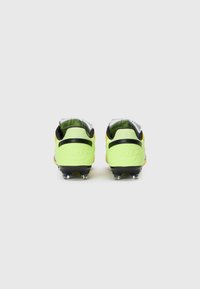Botas de fútbol Nike en amarillo brillante y negro, con una superficie texturizada, acento plateado en el talón y múltiples tacos en la suela.