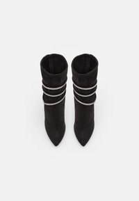 Bottes chevilles en daim noir avec bouts pointus, ornées de trois anneaux en métal argenté autour de la tige. Texture lisse et design élégant.