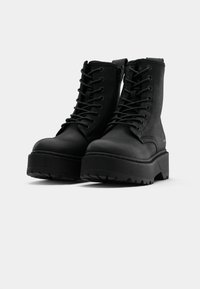 Black lace-up ankle boots with a chunky platform sole, textured matte finish, and side zipper. Treaded outsole for grip and stability.