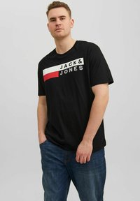 Schwarzes Baumwoll-T-Shirt mit "JACK & JONES"-Logo in Weiß und Rot, kurze Ärmel, lockerer Schnitt, kombiniert mit blauen Jeans.