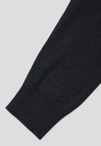 Rękaw ciemnego dzianego swetra z prążkowanym mankietem; materiał wydaje się miękki, z lekko fakturowanym wykończeniem i bezszwowym wzorem.