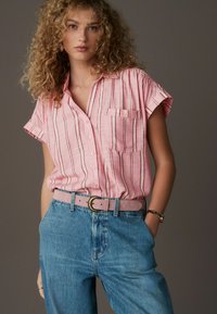 Roze gestreept overhemd met korte mouwen en een zak, gecombineerd met high-waisted blauwe jeans en een lichtroze riem met een ronde gesp.