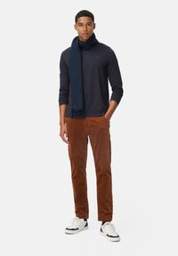 Marine sjaal, lang mouw donker bovenstuk en bruine corduroy broek. Model draagt witte sneakers met marine accenten. Eenvoudig ontwerp, gestructureerde stof.
