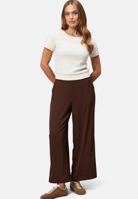 White fitted top with textured pattern, paired with loose brown wide-leg trousers and brown sneakers. Simple, clean design with short sleeves.