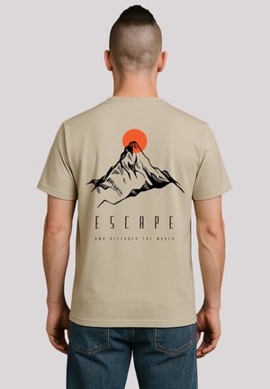 Beige Baumwoll-T-Shirt mit einem schwarzen Berggrafik und einer orangefarbenen Sonne, unten mit dem Text "ENTFLIEHEN UND DIE WELT ENTDECKEN".