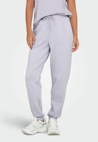 Lichtpaarse joggingbroek met een trekkoord in de taille, elastische boorden en een zachte stof. Gecombineerd met witte sportschoenen.
