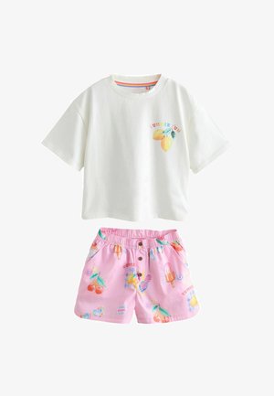 Kind draagt een wit T-shirt en roze korte broek met kleurrijke zomerse prints waaronder kersen, zonnebril, ijsje en citroenen.