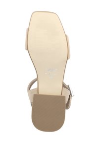 Beige Sandale mit einer strukturierten Gummisohle, schmalem Absatz, verstellbarem Knöchelriemen und minimalem Branding auf derUnterseite.