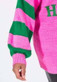 Lengtemouwen gebreide trui met dikke roze en groene horizontale strepen, geribbelde manchetten en een ronde halslijn met glinsterende tekstdetail.