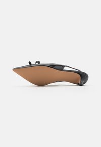 Sorte patentlærredssko med spids tå, slingback-design og lav hæl. Har en lille dekorativ sløjfe og en glat sål.