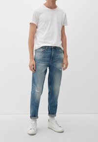 Camiseta blanca de manga corta combinada con unos vaqueros desgastados de color azul claro. El calzado consiste en zapatillas deportivas blancas con detalles en gris.