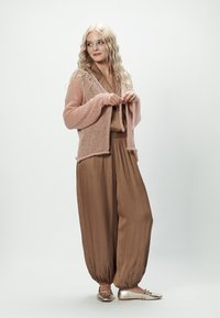 Jasnoróżowy dziergany kardigan nałożony na brązowy satynowy kombinezon o zwężających się nogawkach, w zestawieniu z błyszczącymi złotymi balerinami. Prosty, luźny fason i struktura.