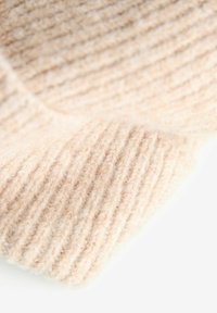 Țesătură tricotată bej cu un model în relief, având o textură moale, care prezintă plieri suprapuse și variații subtile de culoare și grosime.