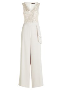 Beżowy kombinezon z błyszczącym, bezrękawnikowym topem i dekoltem w kształcie litery V. Luźna, szeroka nogawka z drapowaną detalem po boku w okolicy talii.