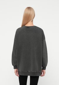 Donkergrijze oversized sweatshirt met lange mouwen, geribde boorden en een ronde hals. Zacht materiaal met een iets versleten textuur.