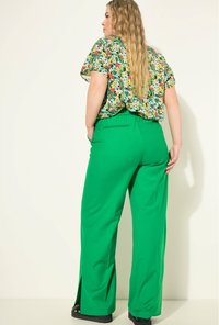 Groene wijde broek met zijsplits en een soepele textuur. Gecombineerd met een kleurrijke top met bloemenprint. Zicht van achter.