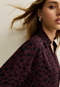 Camicia bordeaux con motivo a cuore nero, design con bottoni e collo classico. Tessuto liscio con vestibilità comoda.