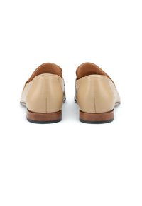 Mocassini in pelle beige con una texture liscia, punta tonda, tacco in legno basso e semplice dettaglio di cucitura sul retro.