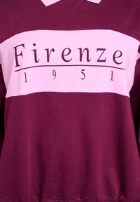 Bordový pulóver s ružovým horizontálnym pruhom. Má grafický text "Firenze" a "1951" v čiernej farbe. Mäkká textúra materiálu, klasický dizajn goliera.