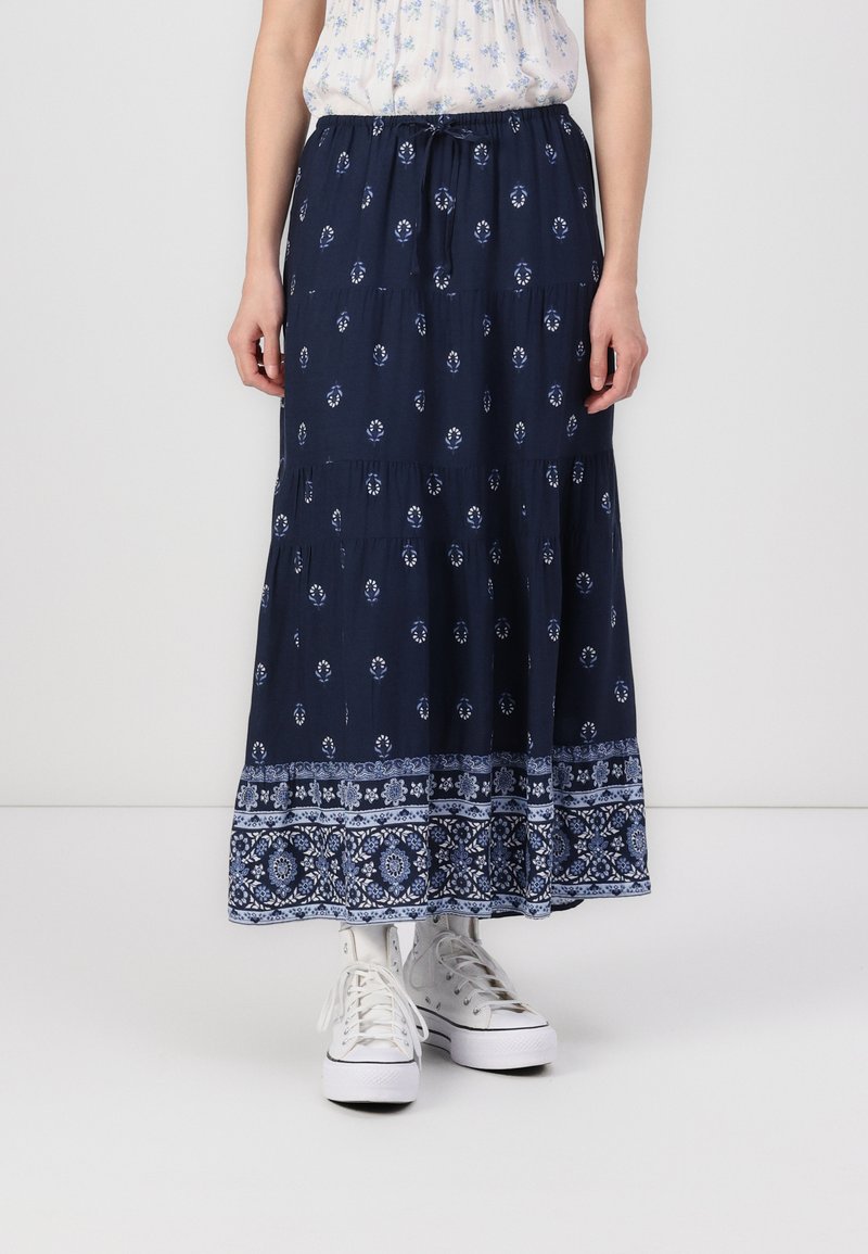 Fustă lungă bleumarin cu modele florale și geometrice albe, având un design în straturi și un talie elastică. Purtați-o cu adidași albi.
