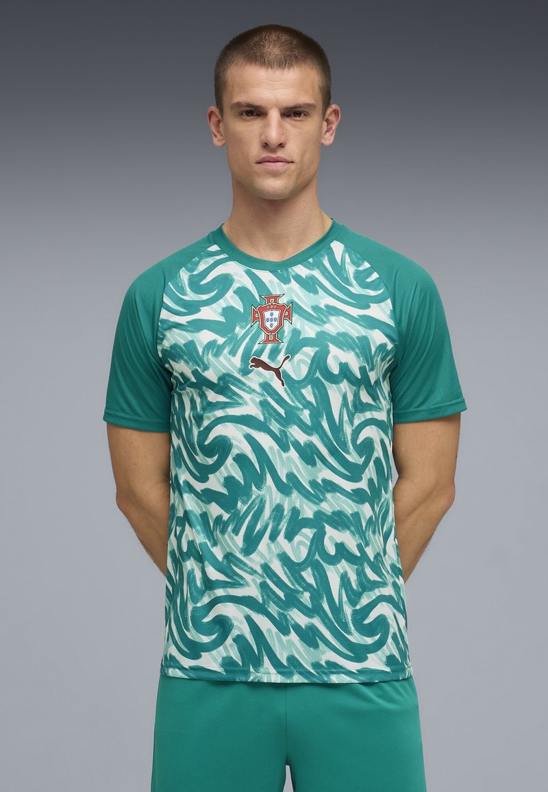 Homme debout, mains dans le dos, portant un maillot de football vert et blanc à motifs du Portugal avec le logo Puma sur la poitrine.