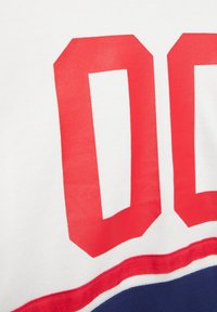 Fehér szövet kiemelkedő piros "00" számmal, texturált mintázattal és alsó részen ívelt, piros és kék varrással.