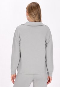 Pullover grigio a trama con un motivo geometrico, dotato di colletto e spalle scese. Il tessuto sembra morbido e leggero.