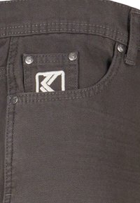 Pilkas audinys kišenėje su sidabro apdaila, turintis baltą logotipo pleistrą ir sustiprintos siuvimo detalės.