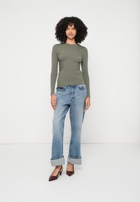 Ριγέ ελιάς πράσινη μπλούζα με μακριά μανίκια σε συνδυασμό με ανοιχτό μπλε παντελόνι φάρδους με γυριστές μανσέτες και μπορντό γόβες με αιχμηρή μύτη.