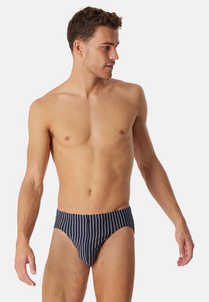 Slip da bagno blu navy con righe verticali bianche, caratterizzati da un design aderente e un tessuto liscio e strutturato.