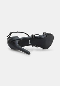 Melnas augstpapēžu kurpes ar gludu ādas apdari, regulējamu siksniņu un dekoratīvām pērlītēm ap potīti. Stilleta papēža dizains.