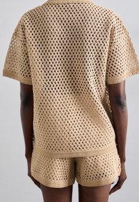 Beige hæklestrikket top og shorts sæt med et diamantmønster. Stoffet er let med en løs pasform og ribkant ved kanterne.