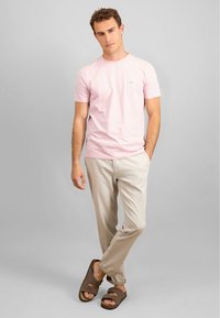 Tricou din bumbac roz pal cu guler rotund, pantaloni din in bej și sandale maro cu talpă plată. Textură netedă, croi lejer, detalii de design minime.