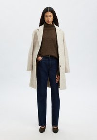 Bežs vilnas mētelis, brūns turtlenecks džemperis, tumši zili džinsi un tumši zaļi papēži. Izstrādājumam ir brīva piegriezuma forma un minimālas aparatūras akcenti.