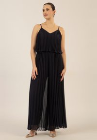 Jumpsuit de navy con pliegues, tirantes finos, cuerpo superpuesto y diseño de pierna ancha. Textura suave; silueta sutilmente fluida.