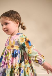 Meerkleurige bloemenjurk van lichtgewicht stof. Lange mouwen, geplooide bovenkant, uitlopende gelaagde rok. Heeft diverse bloemmotieven.