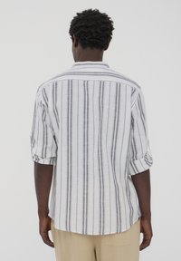 Camicia da uomo a maniche lunghe bianca con righe verticali grigie, caratterizzata da una vestibilità comoda, maniche arrotolabili e un dettaglio sullo sprone posteriore.