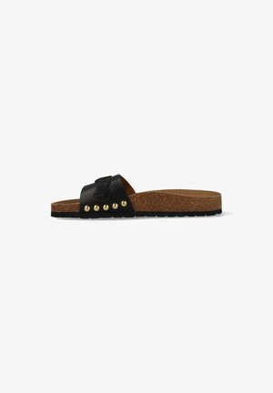 Zwarte slidesandaal met kurken zool, brede leren band, gouden studs en decoratieve stiksels op witte achtergrond, zijaanzicht.