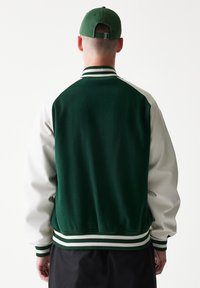 Πράσινο και λευκό varsity μπουφάν με πλεκτό γιακά και μανσέτες, με στιβαρή σκουροπράσινη πλάτη και αντίθετα λευκά μανίκια.