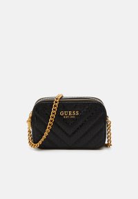 Borsa a tracolla nera trapuntata con catena dorata, caratterizzata da un logo e un motivo a zig zag su materiale lucido, chiusura con zip e forma rettangolare.