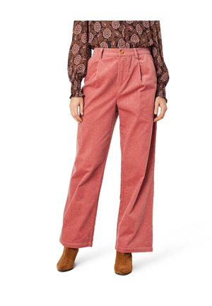 Kvinde iført højttaljede, vidde ben bukser i støvet pink fløjl, blomstret skjorte med lange ærmer og brune ruskindsstøvler til anklen.