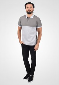 Szürke és világosszürke póló, kétrészes kialakítással, rövid ujjakkal, három gombbal, fekete slim-fit farmernadrággal és fekete sportcipőkkel párosítva.